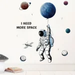 Illustration av en astronaut som håller en ballong som föreställer en planet, med andra himlakroppar runt omkring, åtföljd av texten "I NEED MORE SPACE" för en vetenskaplig och rymdinspirerad dekoration.