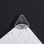Dekorativt föremål i form av Apollo 1969-logotypen, inspirerad av rymdmissionen, placerad på en vit yta med svart bakgrund.