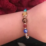 Armband med flerfärgade pärlor och ett charm i guld, bärs på handleden.