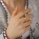 Ring i guld med graverad kemisk symbol, bärs på en persons finger.