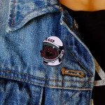 Originalpin i form av en hund med rymdhjälm och inskriptionen "CCCP", fäst på en blå jeansjacka, avslappnad stil.