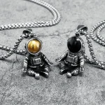 Astronauthäng i metall med gyllene och svarta kulor, hängande på kedjor, designade som original och moderna smycken inspirerade av rymden.