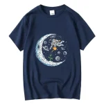 Blå t-shirt med illustration av en astronaut som svävar i rymden, omgiven av planeter, stjärnor och en stiliserad måne, perfekt för vetenskaps- och rymdutforskningsentusiaster.