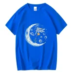 Blå t-shirt med mönster av en astronaut som svävar i rymden, omgiven av planeter, stjärnor och en stiliserad måne. Perfekt för vetenskaps- och astronomientusiaster.