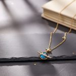 Fantasi-halsband med hängsmycke av planet och stjärna, inspirerat av rymden, i guld och blått, placerat på en mörk yta med en bok i bakgrunden.