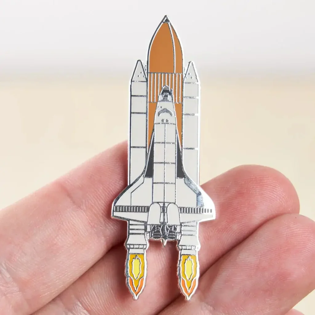 Pin i form av en rymdfarkost med metalldetaljer, som illustrerar en raket redo att lyfta, perfekt för astronomi- och vetenskapsentusiaster.