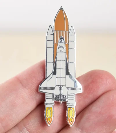 Pin i form av en rymdfarkost med metalldetaljer, som illustrerar en raket redo att lyfta, perfekt för astronomi- och vetenskapsentusiaster.