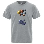 Grå t-shirt med illustration av en astronaut som svävar i rymden under en grupp färgglada planeter. Perfekt för vetenskaps- och astronomientusiaster.