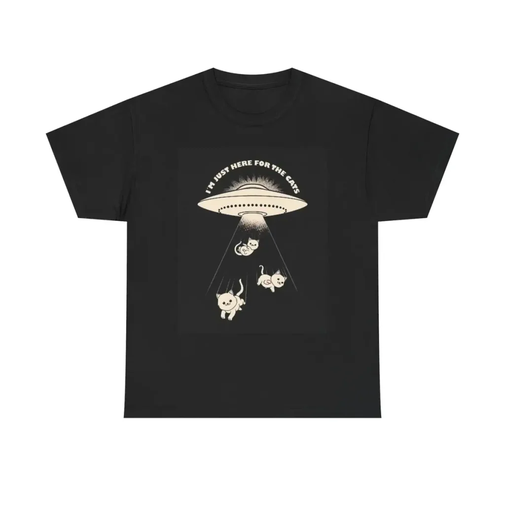 Svart t-shirt med illustration av ett UFO och tre djur under en ljusstråle, texten "I must be here for the cake" högst upp.