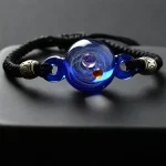 Glasarmband med central sfär som representerar ett kosmiskt universum, prydd med metalliska pärlor och mörkblått glas, perfekt för dekoration eller som vetenskaplig accessoar.
