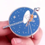 Dekorativ klocka i form av en satellit med blå urtavla och metalliska detaljer.