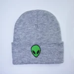 Grå ullmössa med broderad grön alienpatch, perfekt för en avslappnad och original stil. Idealisk för science fiction- och unik designentusiaster.