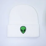 Vit keps med grön och svart alienlogotyp, trendig streetwear-stil.
