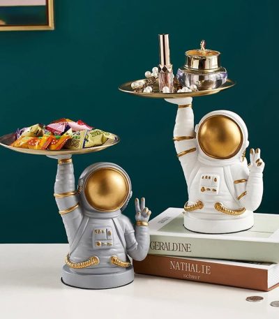 Astronautfigur i vit och guld keramik, använd som dekoration, som håller en bricka med dekorativa föremål och godisar, modern och originalstil.