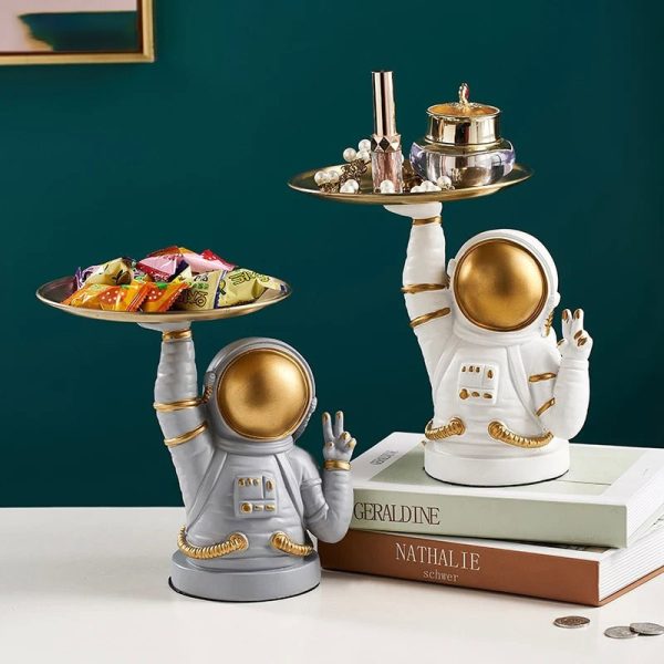 Astronautfigur i vit och guld keramik, använd som dekoration, som håller en bricka med dekorativa föremål och godisar, modern och originalstil.