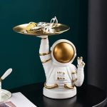Astronautfigur i vit och guld keramik, som håller en bricka med vetenskapliga tillbehör, dekor i kosmisk stil för samling eller inredning.