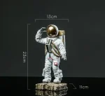 Miniatyrfigur av astronaut med gyllene hjälm, 23,5 cm hög, 13 cm bred och 11 cm djup, idealisk för vetenskaplig eller samlarinredning.