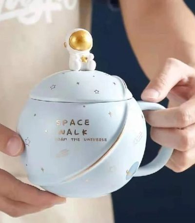 Keramikkopp med rymdmotiv och gyllene astronautfigur på locket, idealisk för dekoration eller konsumtion av rymdinspirerade drycker.