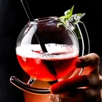 Färgglad cocktail i ett transparent glas med grön garnering, presenterad på en svart bakgrund.