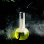 Laboratorievase med en fluorescerande gul vätska och ett glasrör, omgiven av rök, som väcker tankar på ett mystiskt vetenskapligt experiment.
