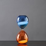 Halsband i form av ett timglas med blå och orange sand, som symboliserar tid och vetenskap, perfekt för dekoration eller som ett originellt vetenskapligt tillbehör.