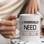 Vit mugg med texten "I PERIODICALLY NEED" och ett periodiskt system som illustrerar kemiska element, perfekt för vetenskaps- och kemiälskare.