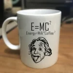 Vit mugg med formeln E=MC², en illustration av en leende Einstein, och frasen "Energy=Milk*Coffee²" för en humoristisk vetenskaplig touch.