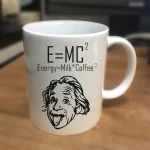 Keramisk mugg med formeln E=MC², en illustration av Einstein och ett humoristiskt citat om energi, mjölk och kaffe.