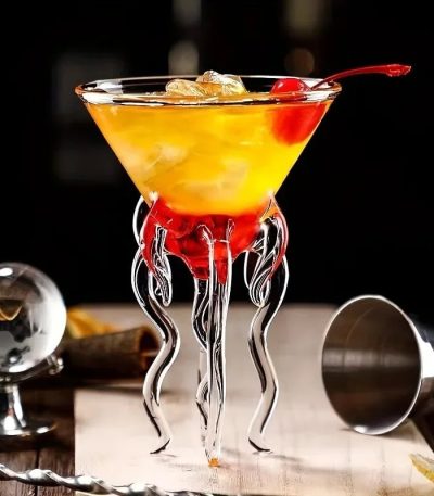 Vetenskapligt cocktailglas med dekoration i form av tentakler i transparent glas, fyllt med en gul-orange cocktail med körsbär, modern baratmosfär.