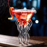 Röd cocktail i ett glas i form av en manet med glas-tentakler, garnerad med apelsin och is, på en träyta, nattlig och mystisk atmosfär.