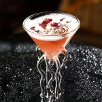 Rosa cocktail i ett glas i form av en flaska med blommiga dekorationer.