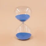 Transparent timglas i glas fyllt med blå sand, symbol för tidens gång, idealiskt för vetenskaplig eller utbildande dekoration.