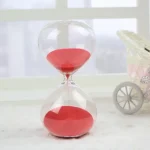 Transparent timglas i glas med röd sand, elegant vetenskaplig dekoration för kontor eller hem.