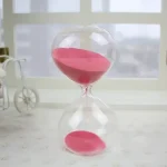 Genomskinlig glasstopp med rosa sand, symboliserar tidens gång, placerad på en ljus yta med minimalistisk bakgrund.
