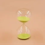 Transparent timglas i glas med grön sand, symbol för tid och tålamod, idealiskt för vetenskaplig dekoration eller som samlarobjekt.