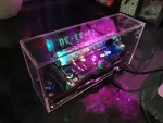 LED-elektronisk displaypanel i ett transparent hölje, visar lysande siffror i blått och grönt, med synliga elektroniska komponenter inuti.