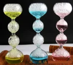 Färgglad glasgunga med luftbubblor, bestående av tre segment i form av bollar, var och en fylld med färgad vätska (gul, blå, rosa) och luftbubblor, på svart bakgrund.