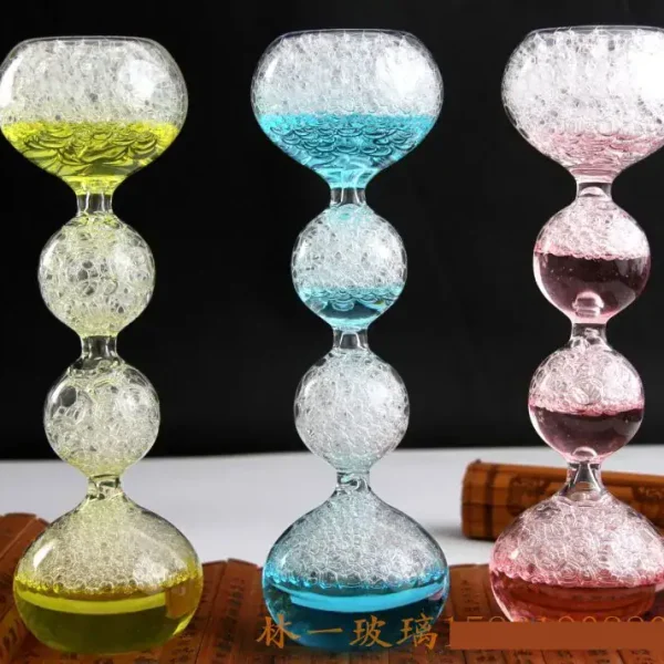 Färgglad glasgunga med luftbubblor, bestående av tre segment i form av bollar, var och en fylld med färgad vätska (gul, blå, rosa) och luftbubblor, på svart bakgrund.