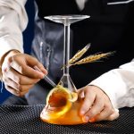 Laboratorieflaska med orange vätska, dekorerad med vete och en sked, som illustrerar vetenskap och forskning.