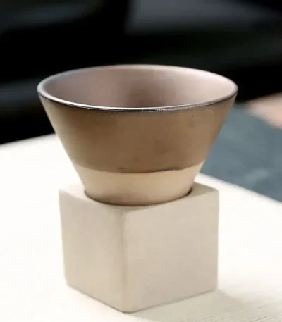 Liten beige keramikkruka placerad på en vit betongbas, idealisk för vetenskaplig eller kontorsdekoration.
