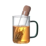 Glasmugg med teinfuser, fylld med varmt vatten som brygger teblad, med en korkpropp placerad ovanpå.