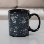 Svart keramikmugg med illustrationer av stjärntecken: Tvillingarna, Skytten, Lejonet, Väduren och fler, med namn på franska.