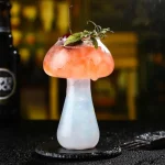 Cocktailglas med färggd dryck och garnering av mynta och körsbär.