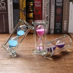 Glas-timglas med färgade sandpulver i rosa, blått och lila, används som vetenskaplig dekoration eller för att mäta tid.