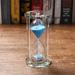 Glas-timglas med blå sand, symboliserar tidens mätning, perfekt för vetenskaplig eller pedagogisk inredning.