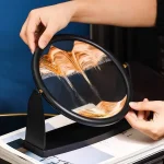 Kinetisk sandpanel i rörelse, som illustrerar en effekt av färgad sandflöde i en svart ram, använd som vetenskaplig och utbildande dekoration.