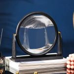 Cirkulärt papperspress i glas med vätska, elegant vetenskapsdekoration, placerad på en bokhög, idealisk för kontors- eller hylldekoration.