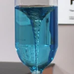 Blå vätskepipett som häller i ett fotat glas, som illustrerar ett vetenskapligt experiment eller en laboratoriedemonstration.