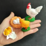 Vit plastkyckling med röd kam, vita ägg i ett orange bo, liten gul kyckling på ett krossat ägg, dekorativa figurer för vetenskapligt eller utbildningsämne.