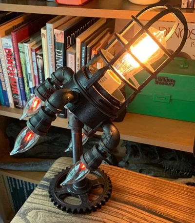 Designad skrivbordslampa inspirerad av en raket med varmt ljus och svart metallstruktur. Perfekt för modern eller tematisk vetenskaplig dekoration.